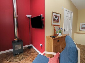 A room with a red wall, a wooden cabinet, a blue sofa, a small heater, a TV mounted on the wall, and a door. - Tirlaggan Studio (Oban)