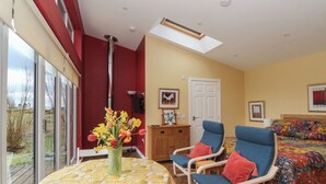 A room with a yellow patterned table, two blue chairs, a bed with a colorful blanket, a wooden cabinet, and a door. - Tirlaggan Studio (Oban)