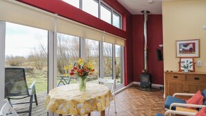 A room with a large window, a table with a yellow tablecloth, a chair, a sofa, a fireplace, and a painting on the wall. - Tirlaggan Studio (Oban)