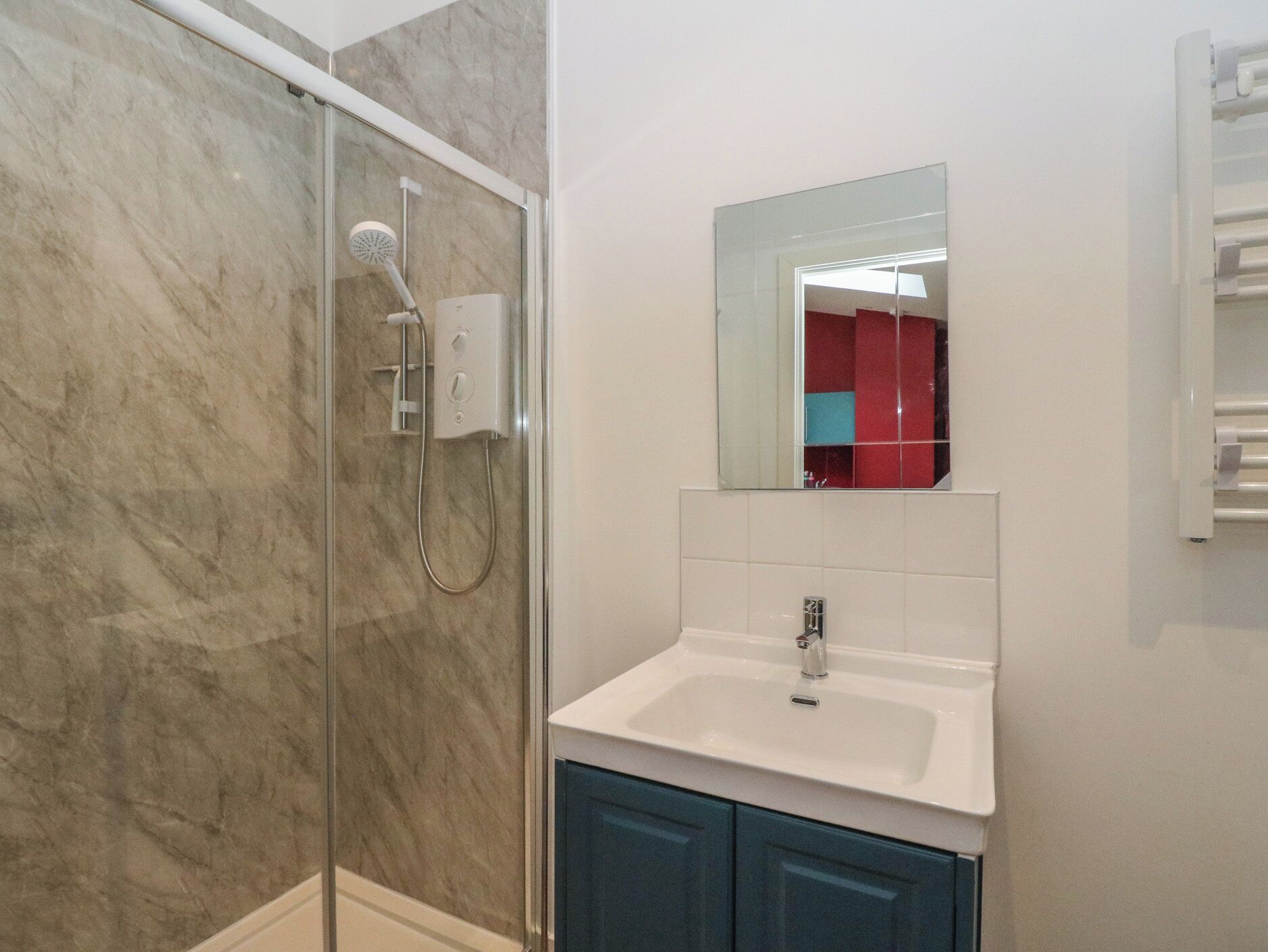 A modern bathroom with a glass-enclosed shower, a white sink, and a mirror above it.