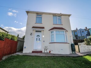 A two-story residential building with a white facade, a bay window, and a front door with a small porch. - Hilltop Cottage (Paignton)