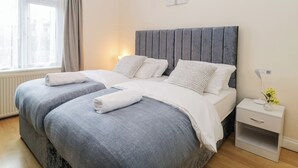 A modern bedroom with a large bed, two bedside tables, a nightstand, and a window with curtains. - Hilltop Cottage (Paignton)