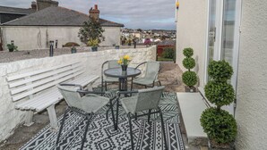 A patio with a round table and chairs, a white bench, and potted plants. - Hilltop Cottage (Paignton)