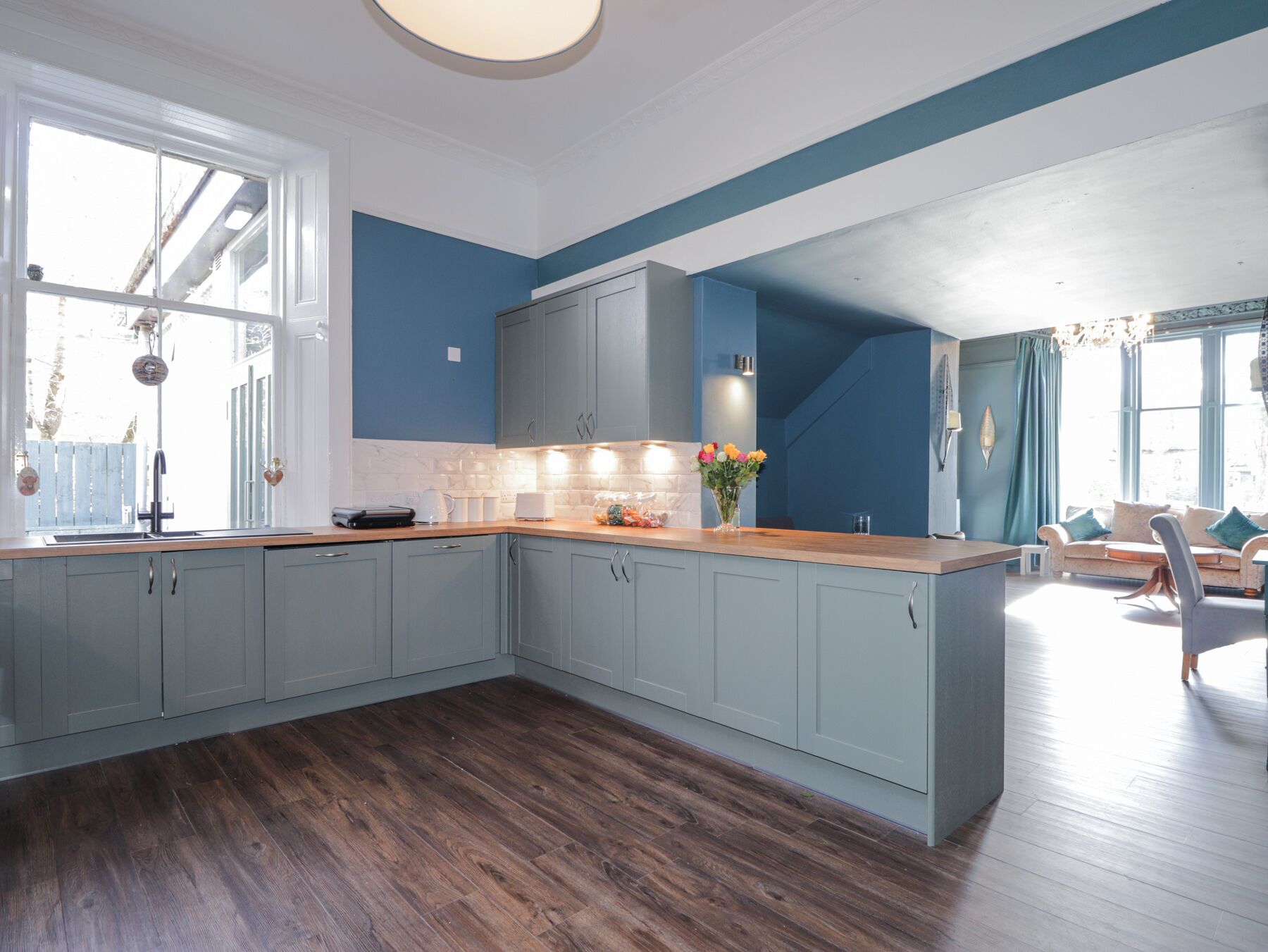 A modern kitchen with grey cabinets, a wooden countertop, and a large window.