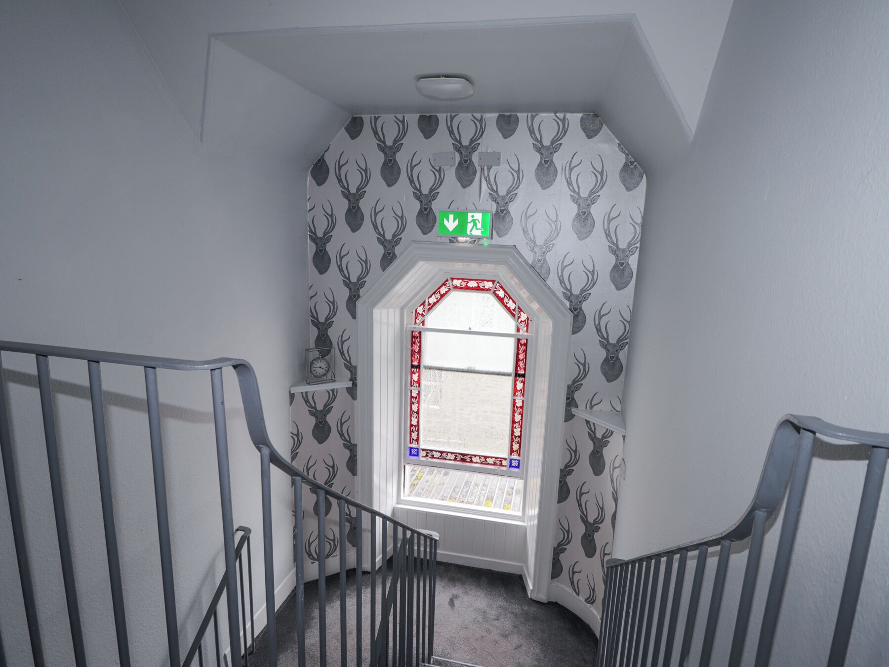 A staircase with a patterned wall, a window with a red frame, and a green exit sign.