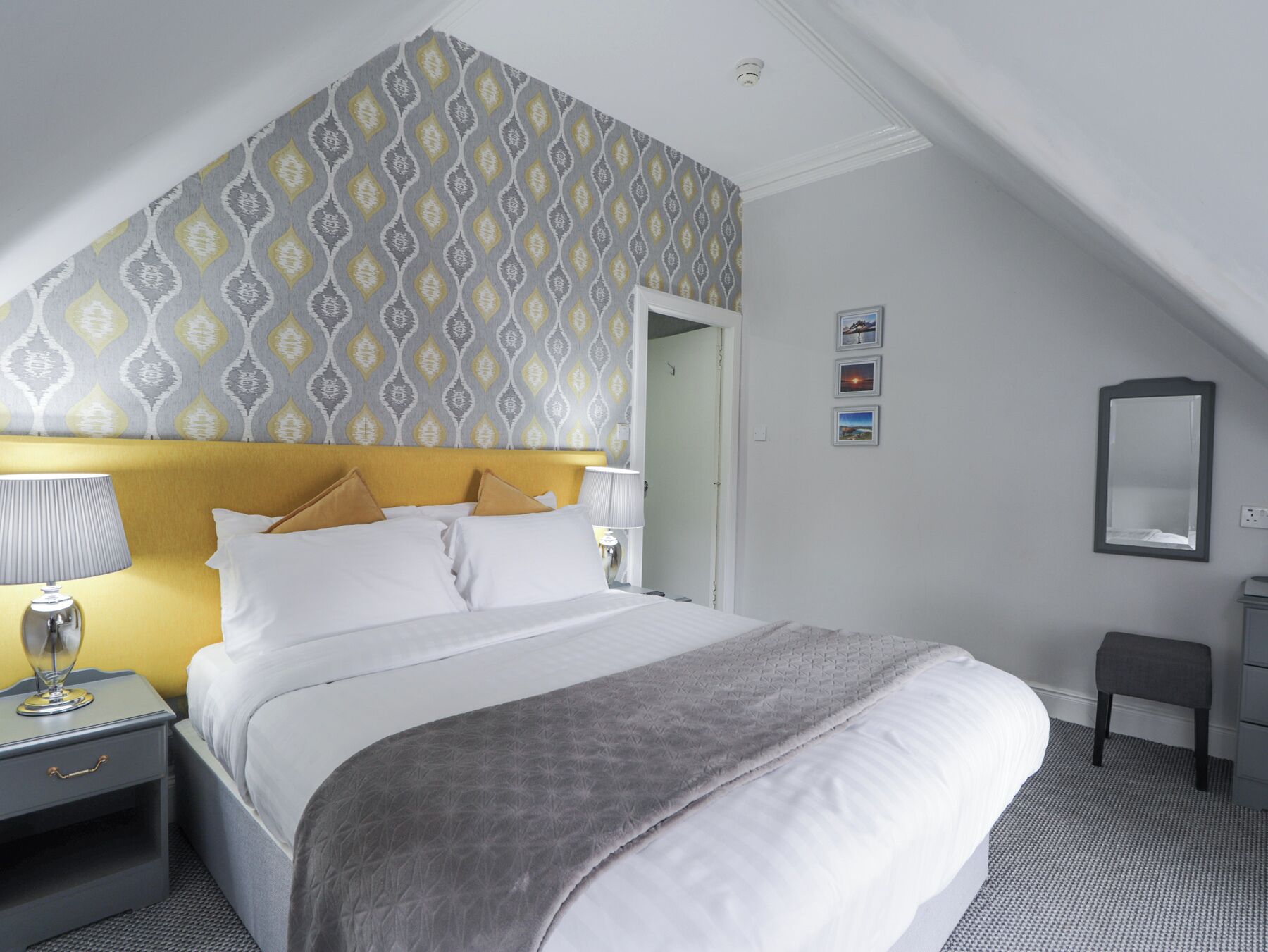 A hotel room with a bed, bedside tables, a lamp, a mirror, and a patterned wallpaper.