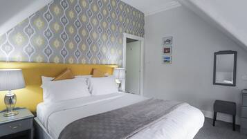A hotel room with a bed, bedside tables, a lamp, a mirror, and a patterned wallpaper.
