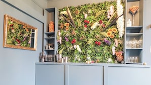 A bar area with a green wall adorned with flowers and plants, shelves with glasses and bottles, and a framed mirror on the wall. - Glenspey (Kingussie)