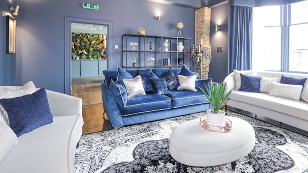 A blue-themed living room with a blue sofa, white armchairs, a white ottoman, and a patterned rug. - Glenspey (Kingussie)