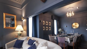 A modern living room with a white sofa, blue and white cushions, a dining area with a table set for six, and a chandelier. - Glenspey (Kingussie)
