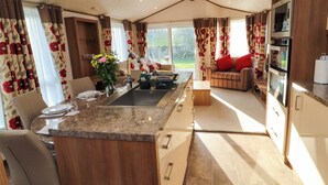 A spacious kitchen with a central island, wooden cabinets, and a large window offering a view of the outdoors. - Lodge 4 (Carnforth)