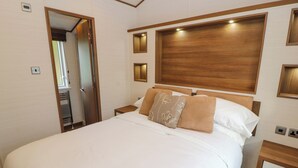 A hotel room with a large bed, wooden headboard, bedside tables, and a wardrobe. - Lodge 4 (Carnforth)