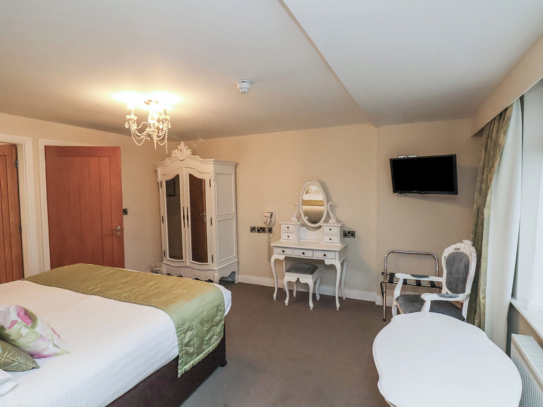 Une chambre d’hôtel avec un lit, un bureau doté d’un miroir, une chaise, une armoire et un téléviseur fixé au mur.