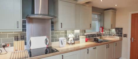 A modern kitchen with light-colored cabinets, a stainless steel range hood, a built-in oven, and a wooden countertop.