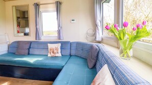 Ein modernes Wohnzimmer mit einem blauen Modulsessel, einem Spiegel, einem Fenster mit Vorhängen und einer Vase mit Tulpen.