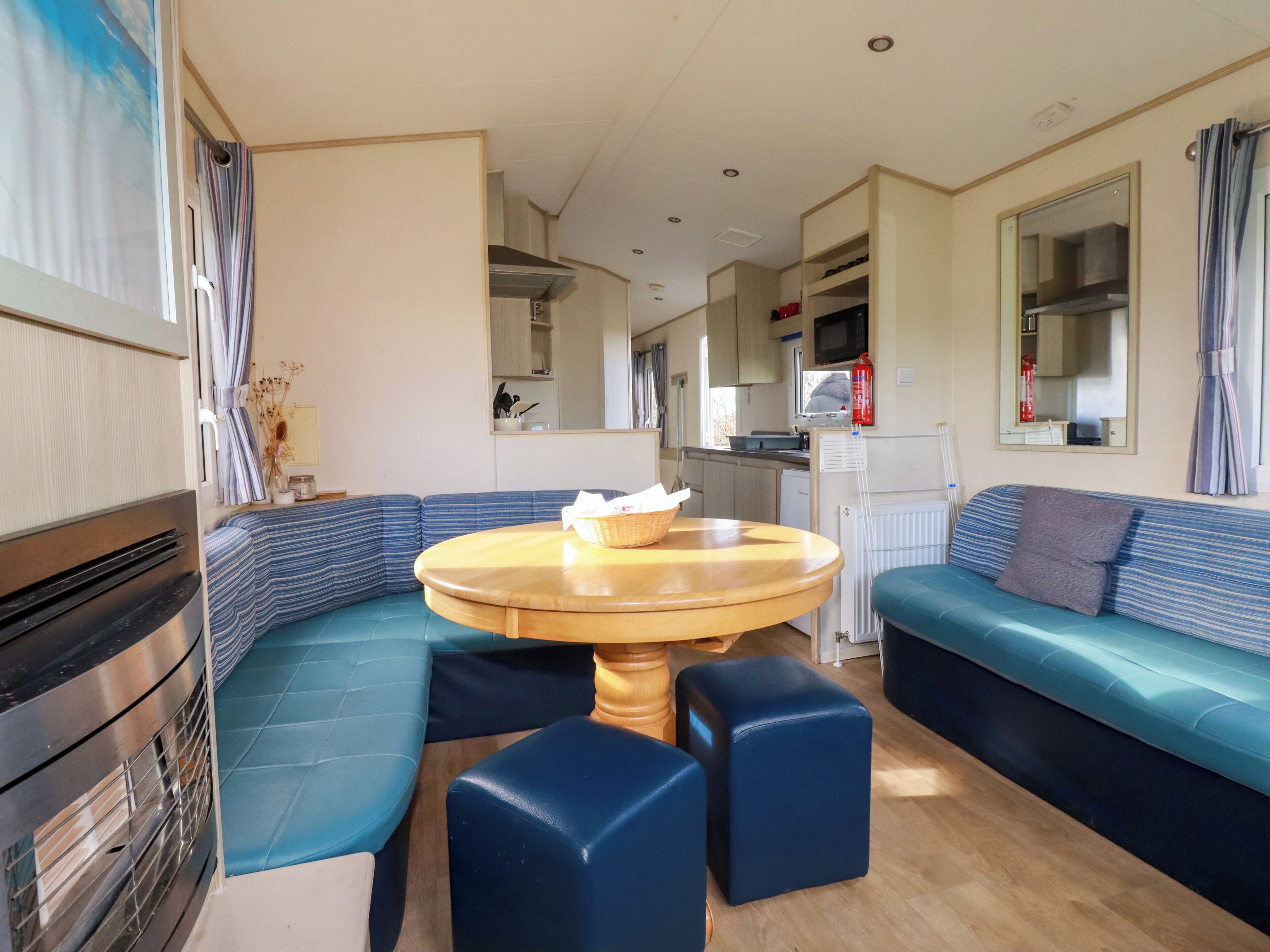 A modern RV interior with a dining area, seating, kitchenette, and a large mirror.
