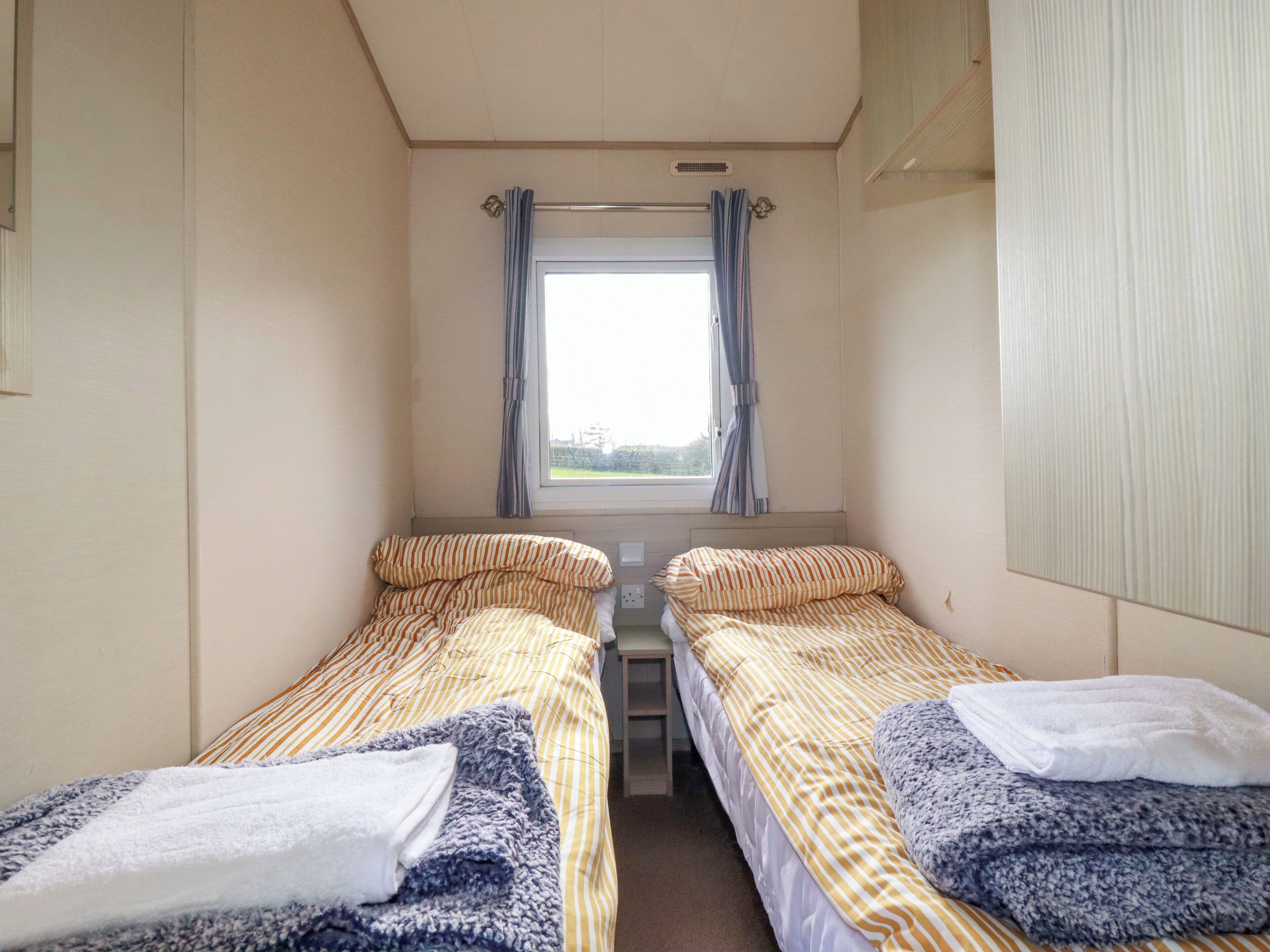 A small, single-room accommodation with two beds, a window with curtains, and a radiator above the window.