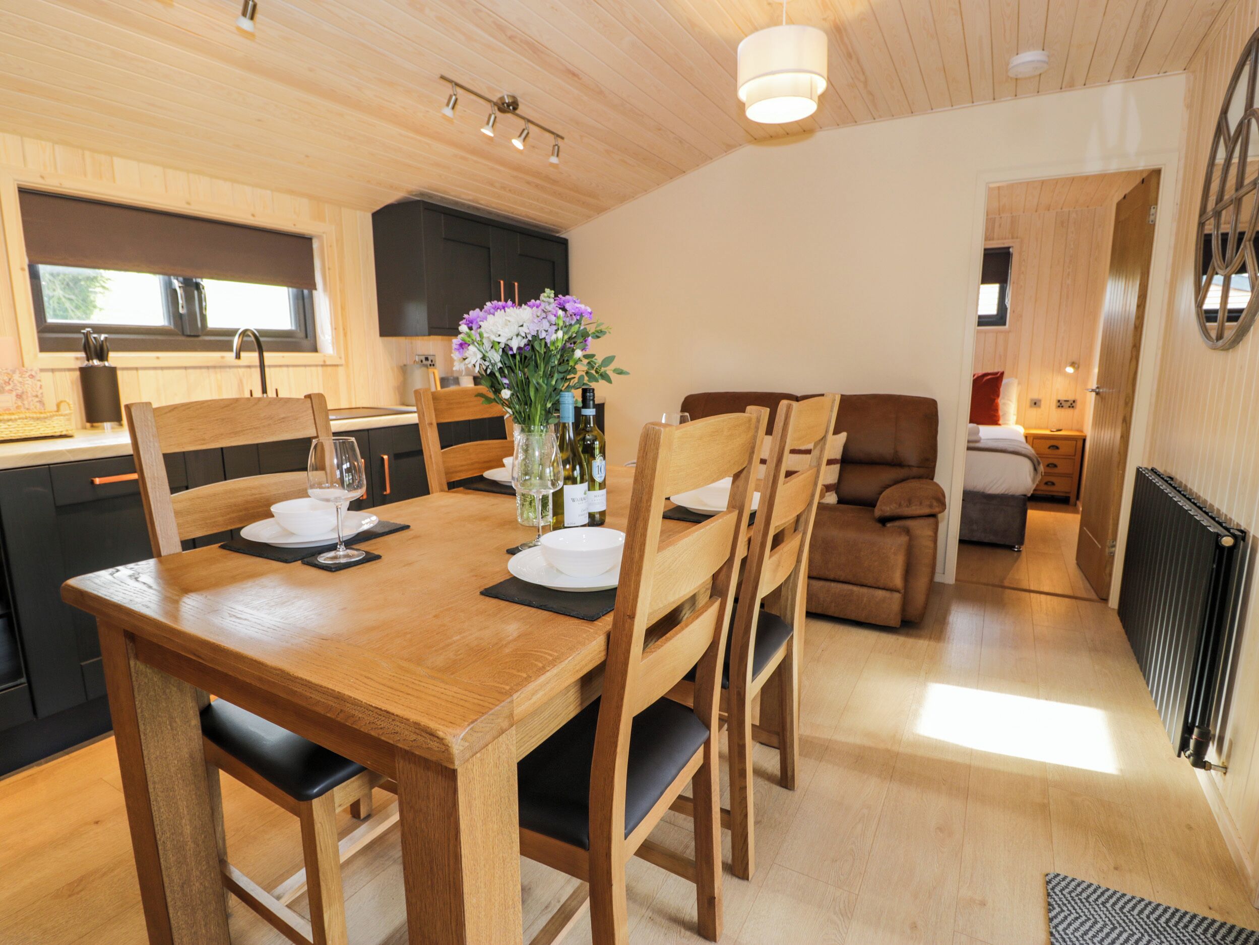 A wooden dining table with chairs, a vase with flowers, and a kitchen in the background.
