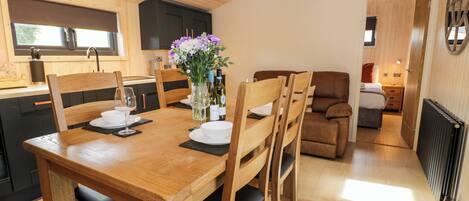 A wooden dining table with chairs, a vase with flowers, and a kitchen in the background.