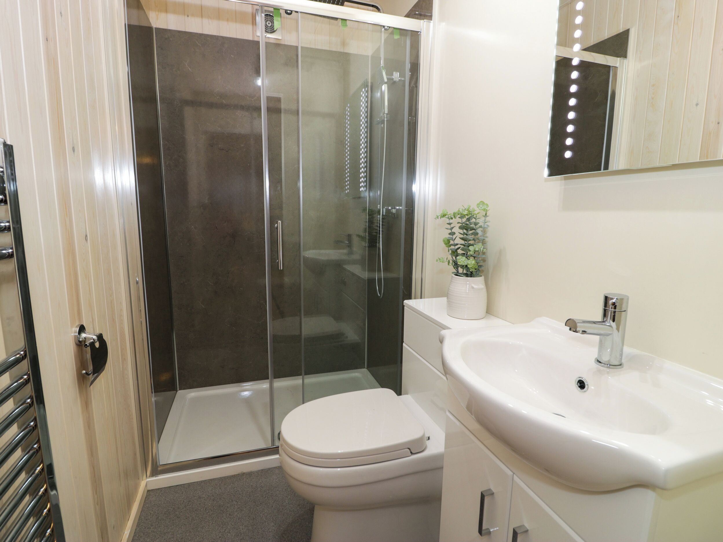 A modern bathroom with a glass-enclosed shower, a white toilet, a sink with a mirror, and a potted plant on the vanity.