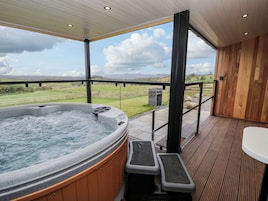 Un jacuzzi con revestimiento de madera, una terraza de madera y vistas a un paisaje cubierto de césped.