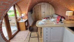 A cozy kitchen with a brick arch, wooden cabinets, and a dining area with a table set for two. - Weirglodd (Ruthin)