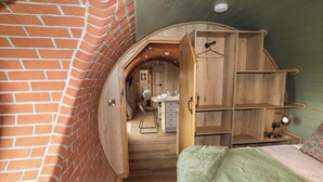 A loft-style bedroom with a brick wall, wooden shelves, and a view into the kitchen. - Weirglodd (Ruthin)