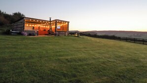A rustic wooden structure with string lights, a barbecue area, and a view of the landscape.