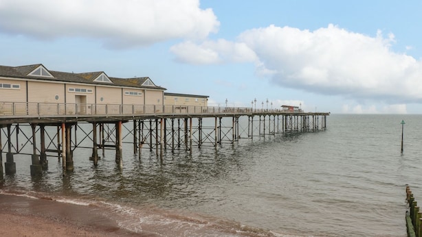 Un muelle se extiende sobre aguas tranquilas, con una hilera de edificios al final.