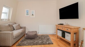 Una sala de estar con un sofá, un reposapiés, un mueble de madera y un televisor de pantalla plana.