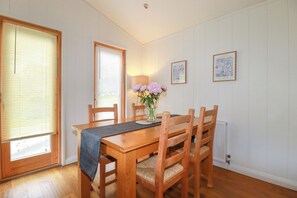 A dining area with a wooden table and chairs, a vase with flowers, and two framed pictures on the wall. - 10 Water's Edge (Looe)