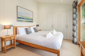 A neatly made bed with white linens and pillows, a bedside table with a lamp, a painting on the wall, and a wardrobe. - 10 Water's Edge (Looe)