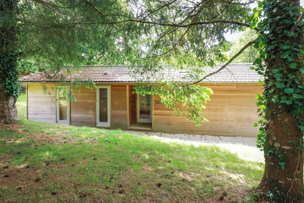 A wooden cabin with a tiled roof, a door, and a window. - 10 Water's Edge (Looe)