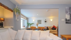 Un salon avec un canapé blanc, une table à manger avec des chaises, une statue de Bouddha et une horloge au mur.