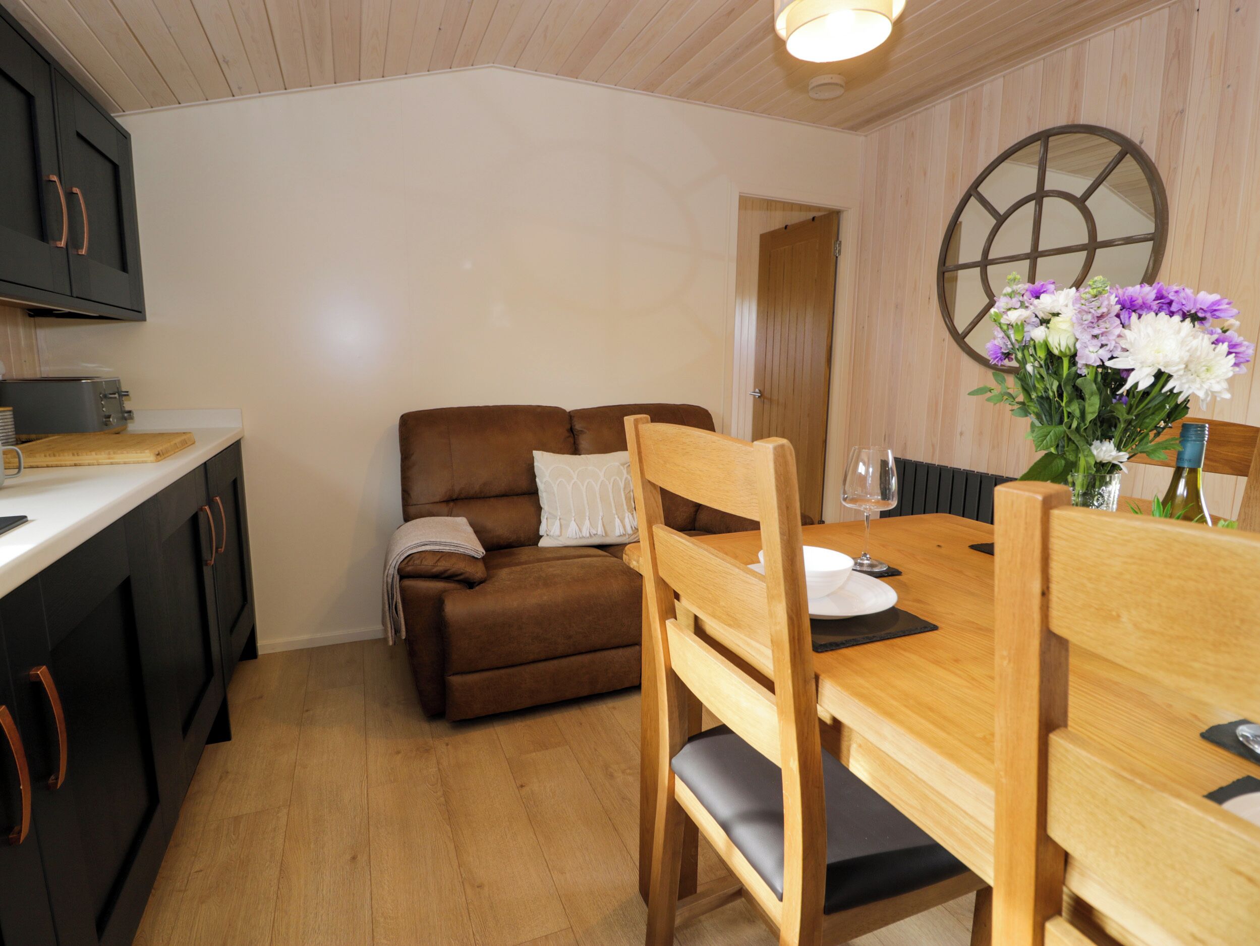 A cozy living area with a brown sofa, wooden dining table, and a vase of flowers.
