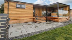 A modern wooden house with a covered patio, stone flooring, and a brick wall.