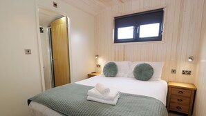 A neatly made bed with a green quilt, a window above it, and a wooden nightstand with drawers.