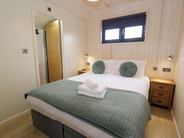 Una cama bien tendida con un edredón verde, una ventana encima y una mesita de noche de madera con cajones.