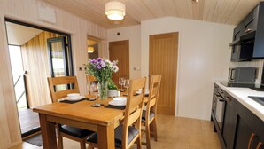 A wooden dining table with four chairs, a vase with flowers, and a kitchen area with cabinets and a microwave.