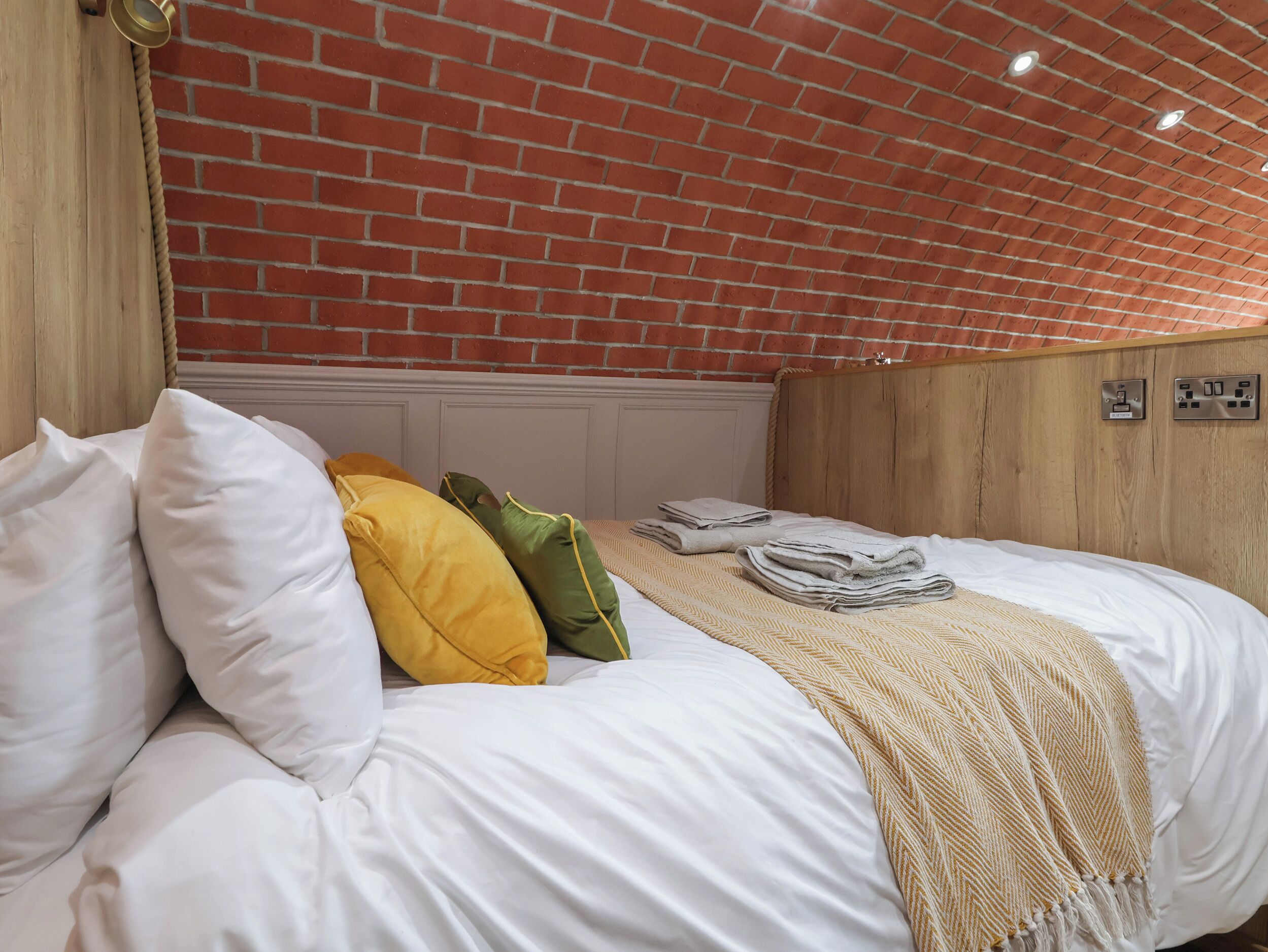 Een net opgemaakt bed met witte en gele kussens, een beige deken en een houten hoofdbord.