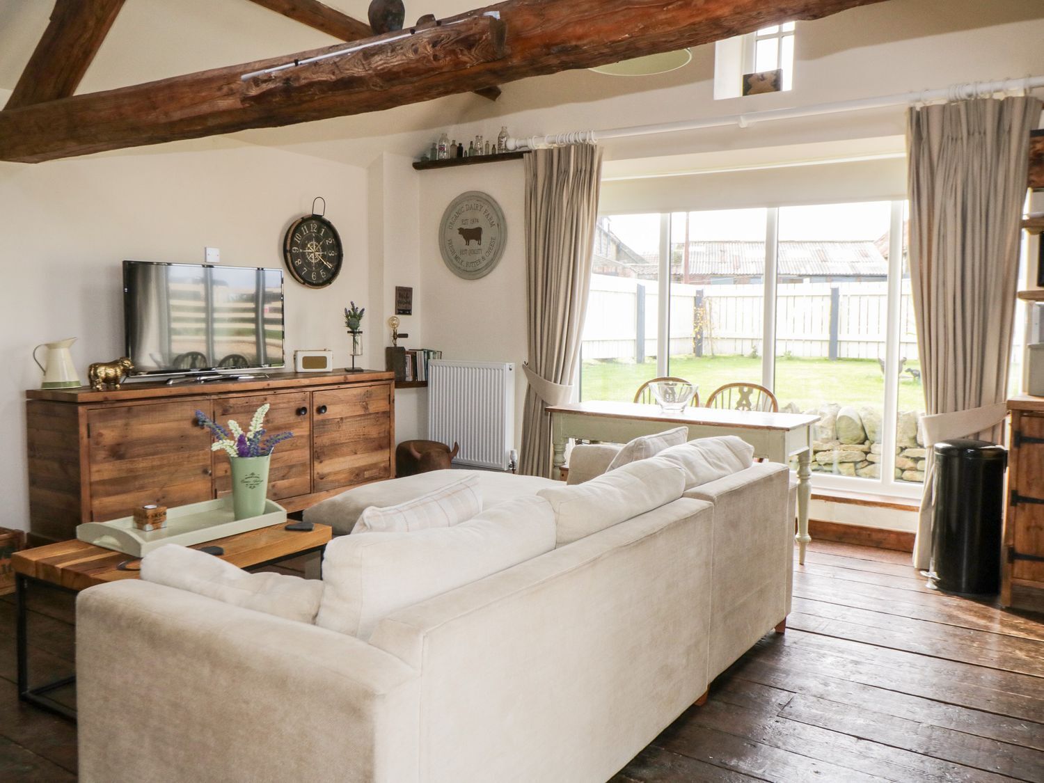 Un salon chaleureux avec un grand canapé, des meubles en bois, un téléviseur et une fenêtre avec des rideaux.