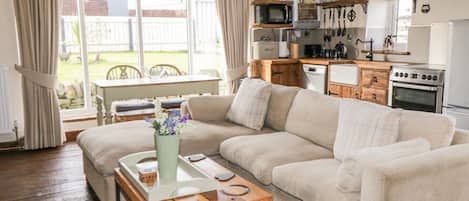 A cozy living room with a sofa, a wooden coffee table, and a view of the backyard through large windows.