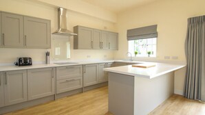 A modern kitchen with grey cabinets, a central island, and a window with curtains. - Cheltenham Cottage (Oswestry)