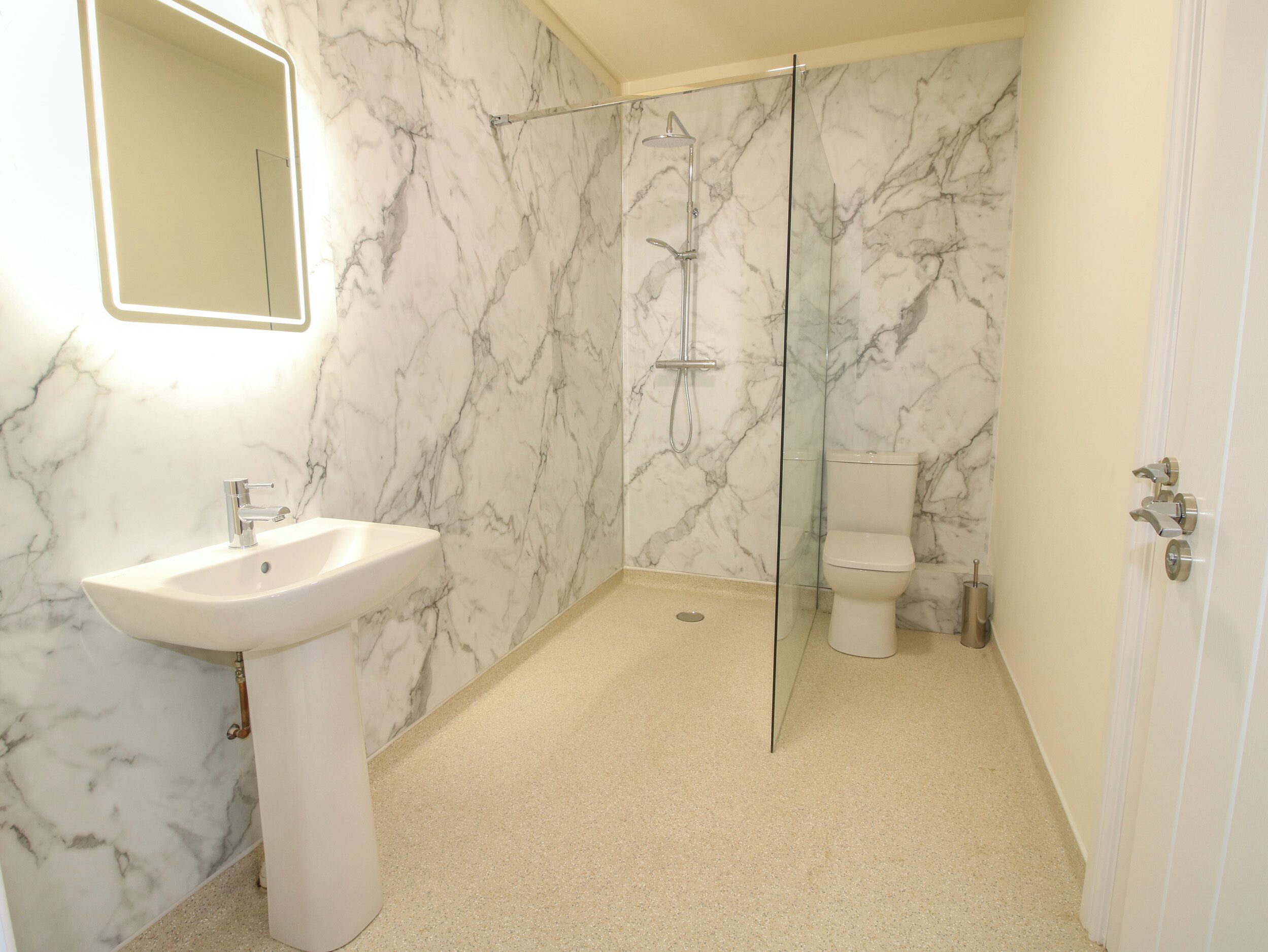 A bathroom with a marble wall, a glass shower enclosure, a white sink, and a toilet.