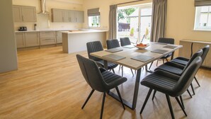 A modern kitchen with a central island, a dining area with six chairs, and a large window with curtains. - Cheltenham Cottage (Oswestry)