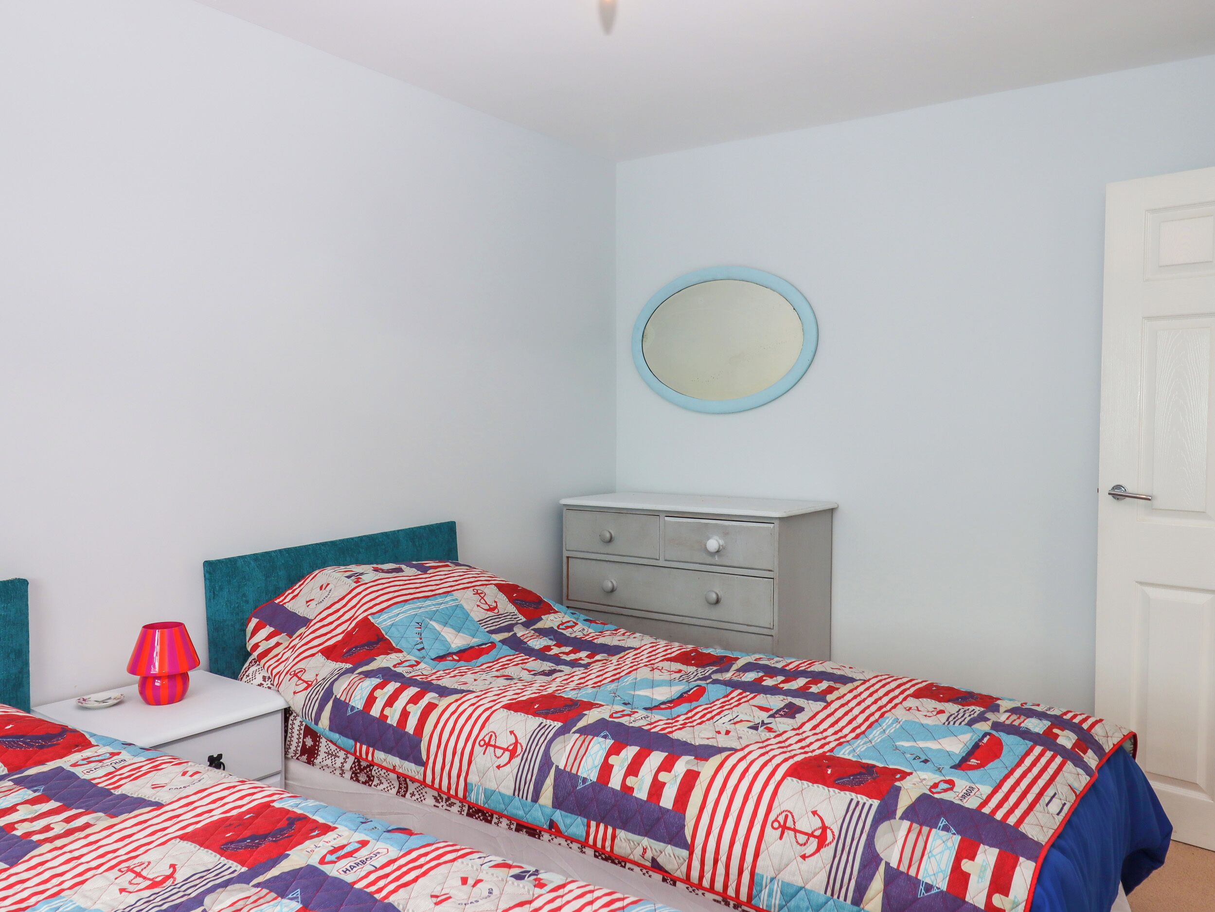 A bedroom with two beds, a dresser, a nightstand, a lamp, and a mirror.