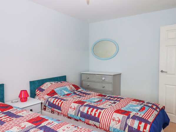 A bedroom with two beds, a dresser, a nightstand, a lamp, and a mirror. - Brixham Breeze Cabin (Brixham)