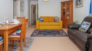 Un salon avec un canapé jaune, un canapé en cuir marron, une table à manger avec des chaises, un meuble en bois et un tapis.