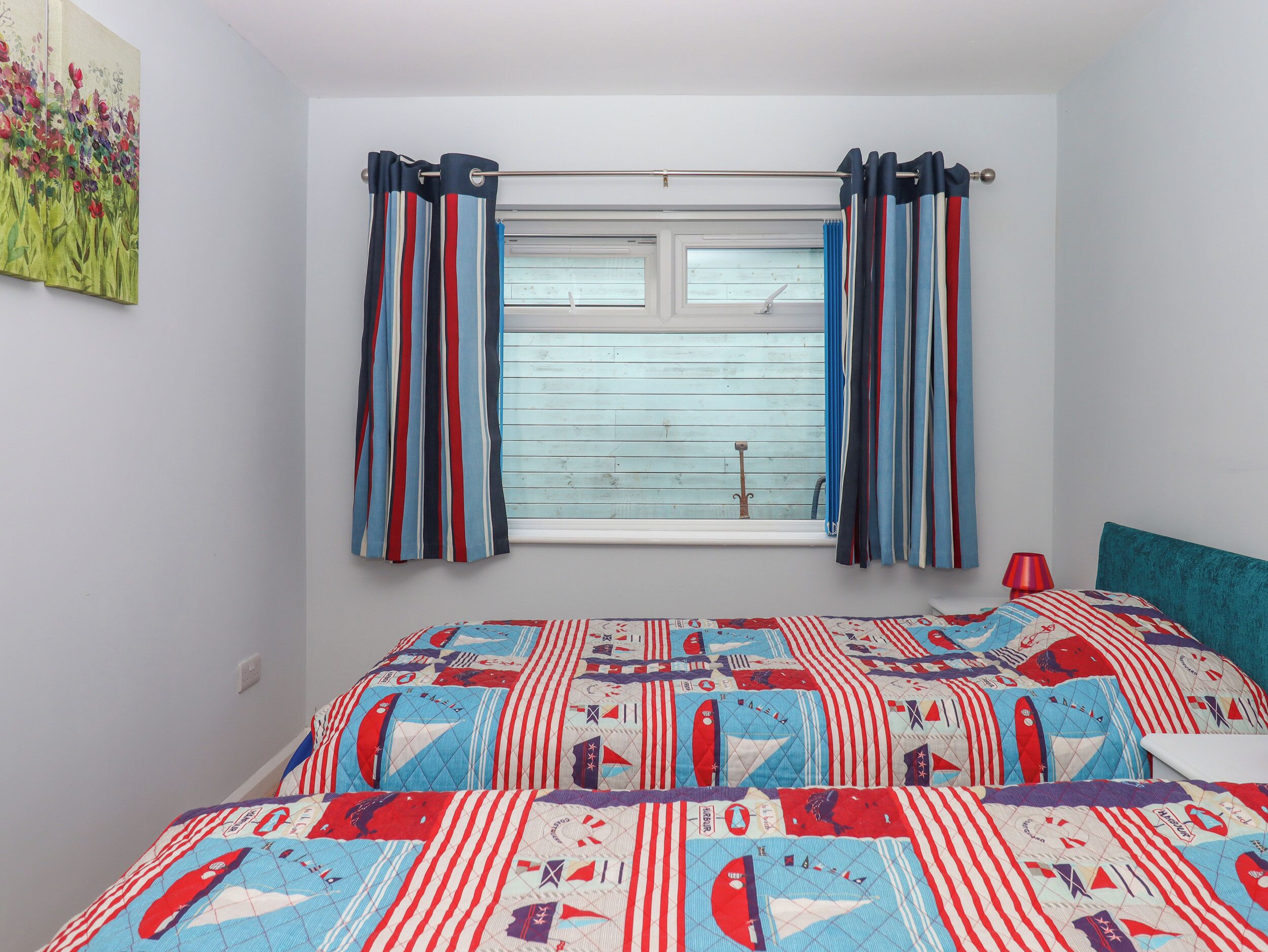 A bedroom with a bed covered in a patterned quilt, a window with striped curtains, and a wall with a floral painting.