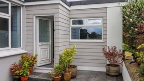 Une maison d’habitation à l’extérieur gris, avec une porte d’entrée et un petit porche agrémenté de plantes en pot.